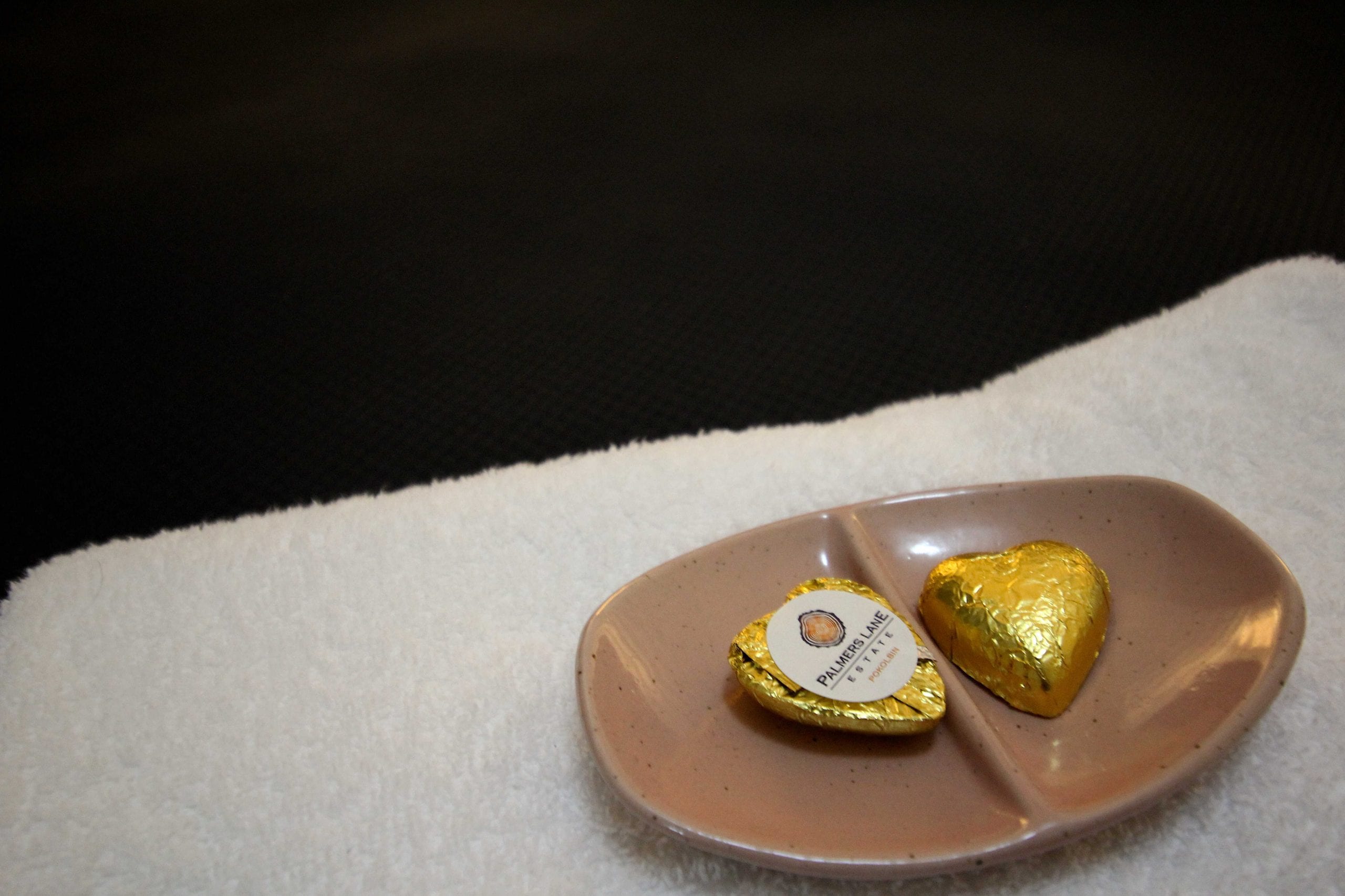Close up of two gold wrapped chocolates with Palmers Lane Estate logos placed on a plate