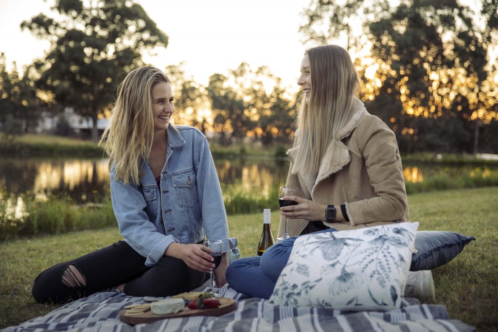 friends laughing on picnic rug drinking wine